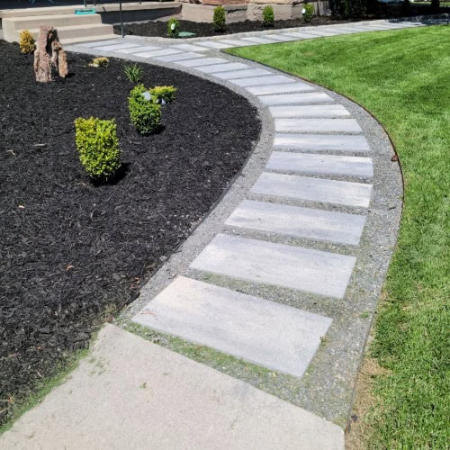 Walkway with concrete pavers, garden bed with fresh mulch and small shrubs on the left, a manicured lawn on the right.